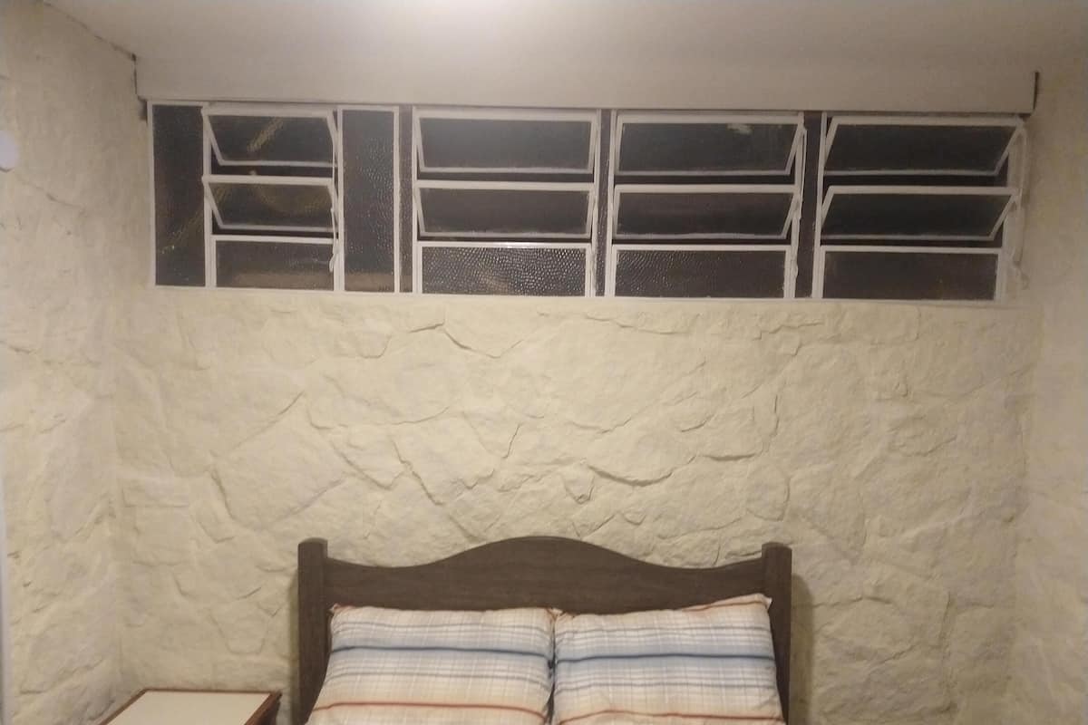 Una habitación con cama, mesita de noche y ventana de varios paneles.