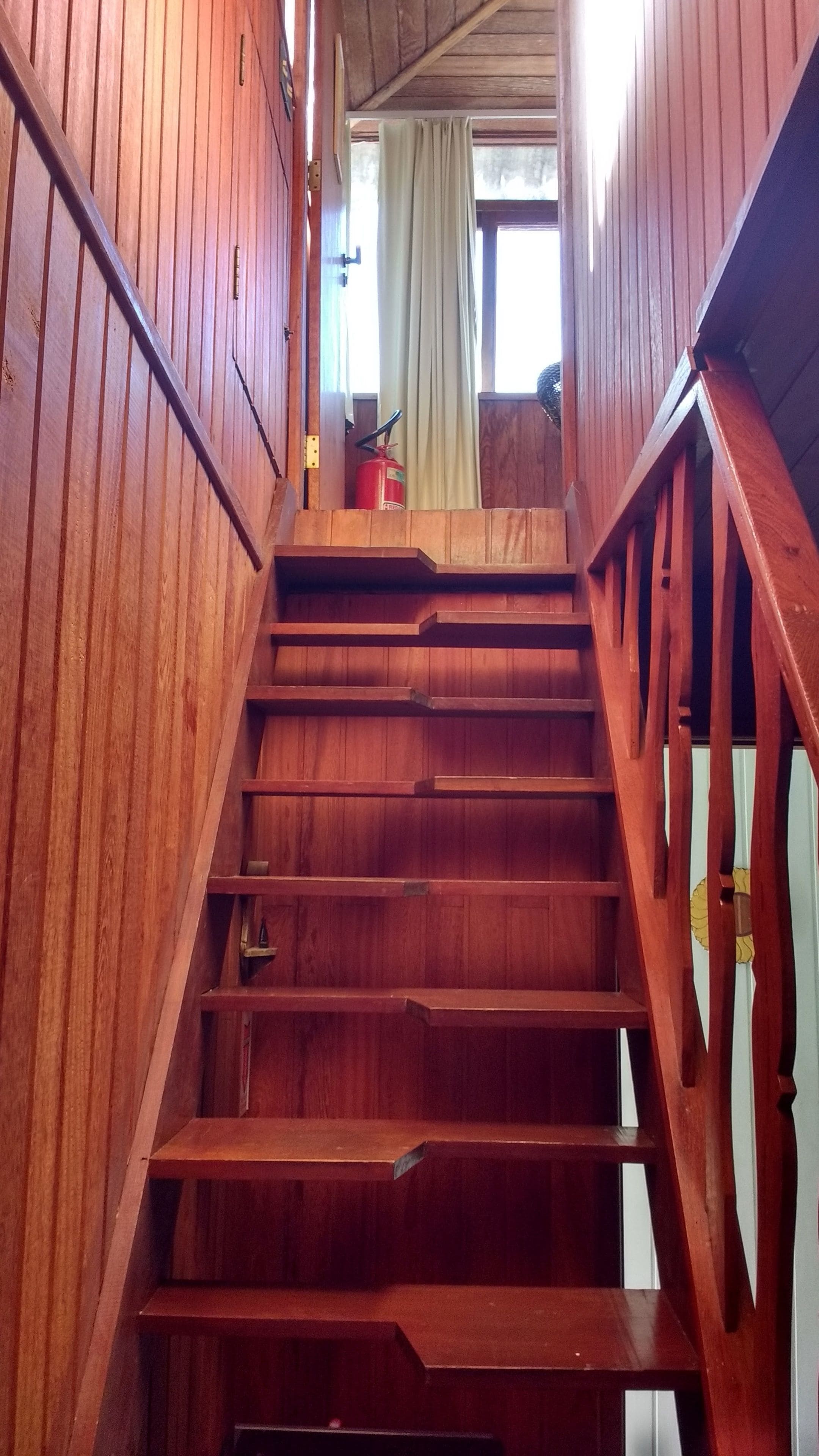 A wooden staircase with a metal handrail and a fire extinguisher at the top.