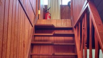 A wooden staircase with a metal handrail and a fire extinguisher at the top.