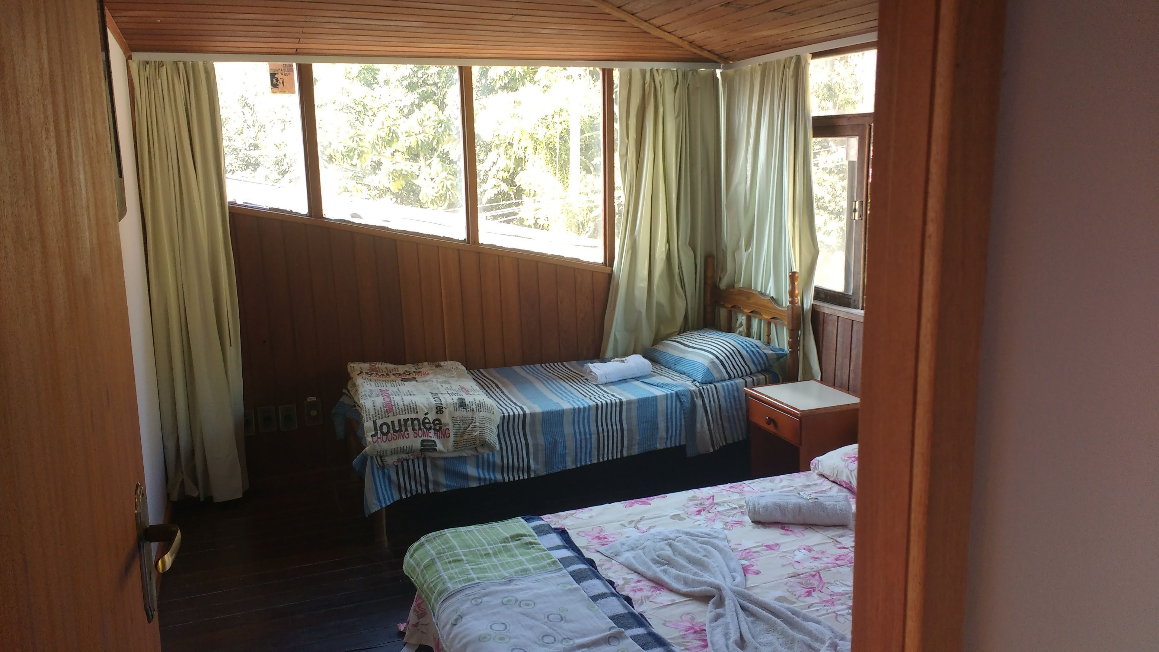 A small, cozy room with two beds, wooden walls, and a window with curtains.
