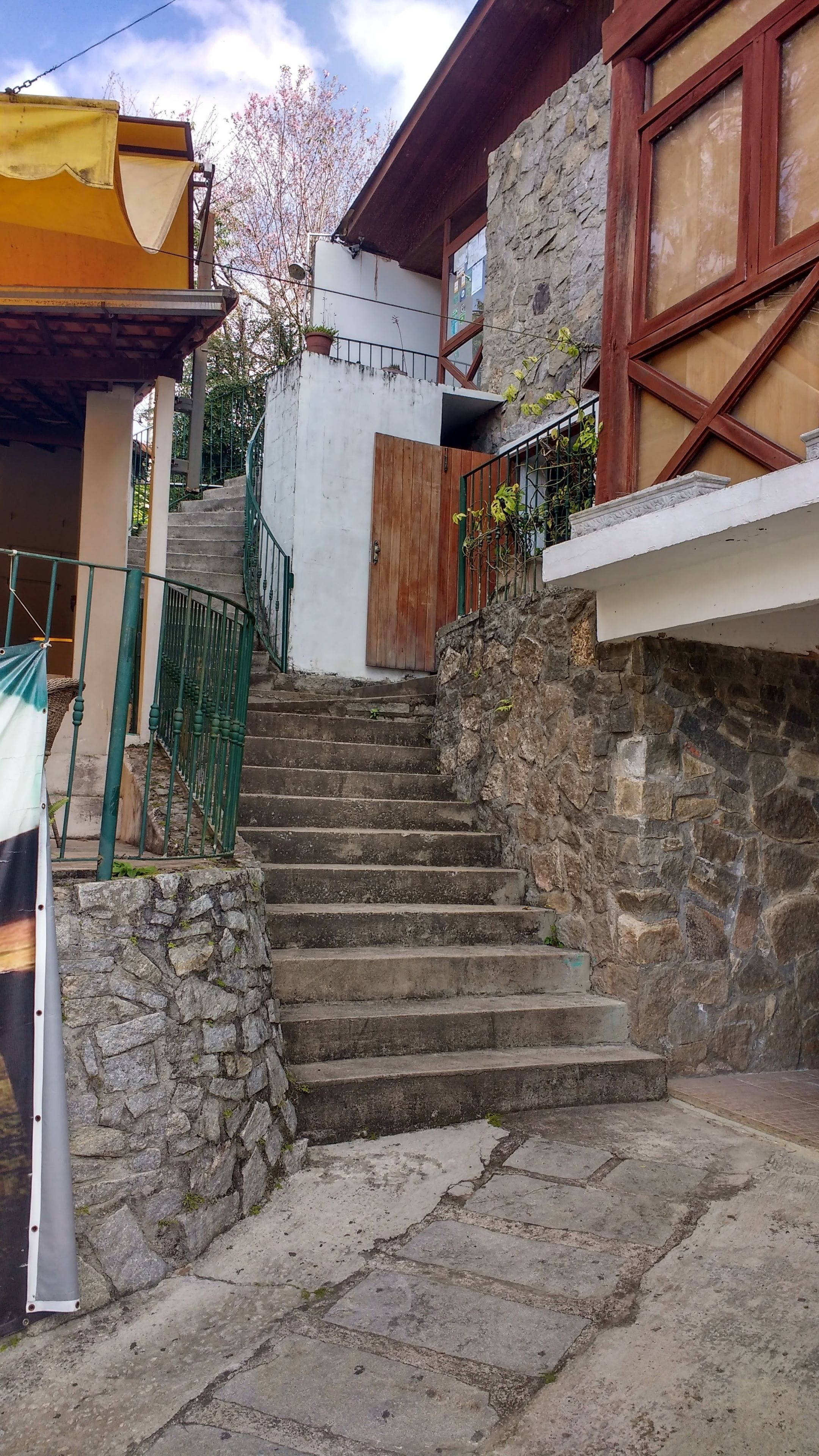 Una escalera de piedra que lleva a una puerta de madera, rodeada de muros de piedra y una barandilla de metal.