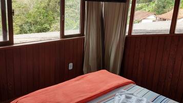 Una habitación con cama, ventana con cortinas y vistas a zonas verdes y una montaña.