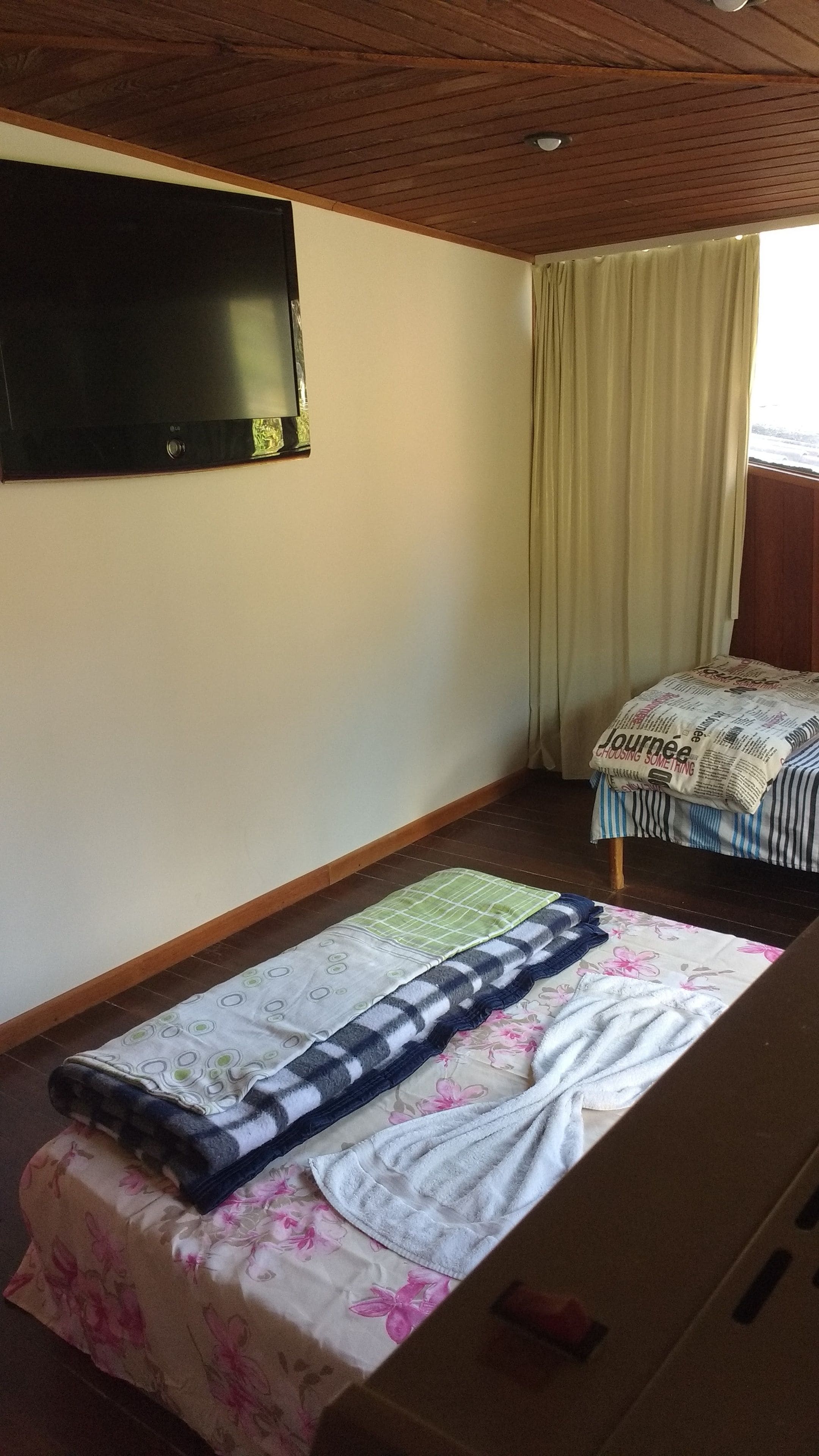 A room with a bed, a television on the wall, and a window with curtains.