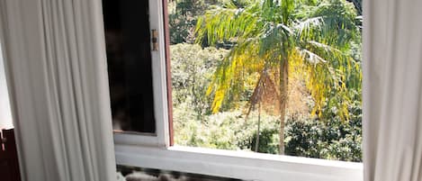 Una habitación con cama, ventana con cortinas y vista a zonas verdes.