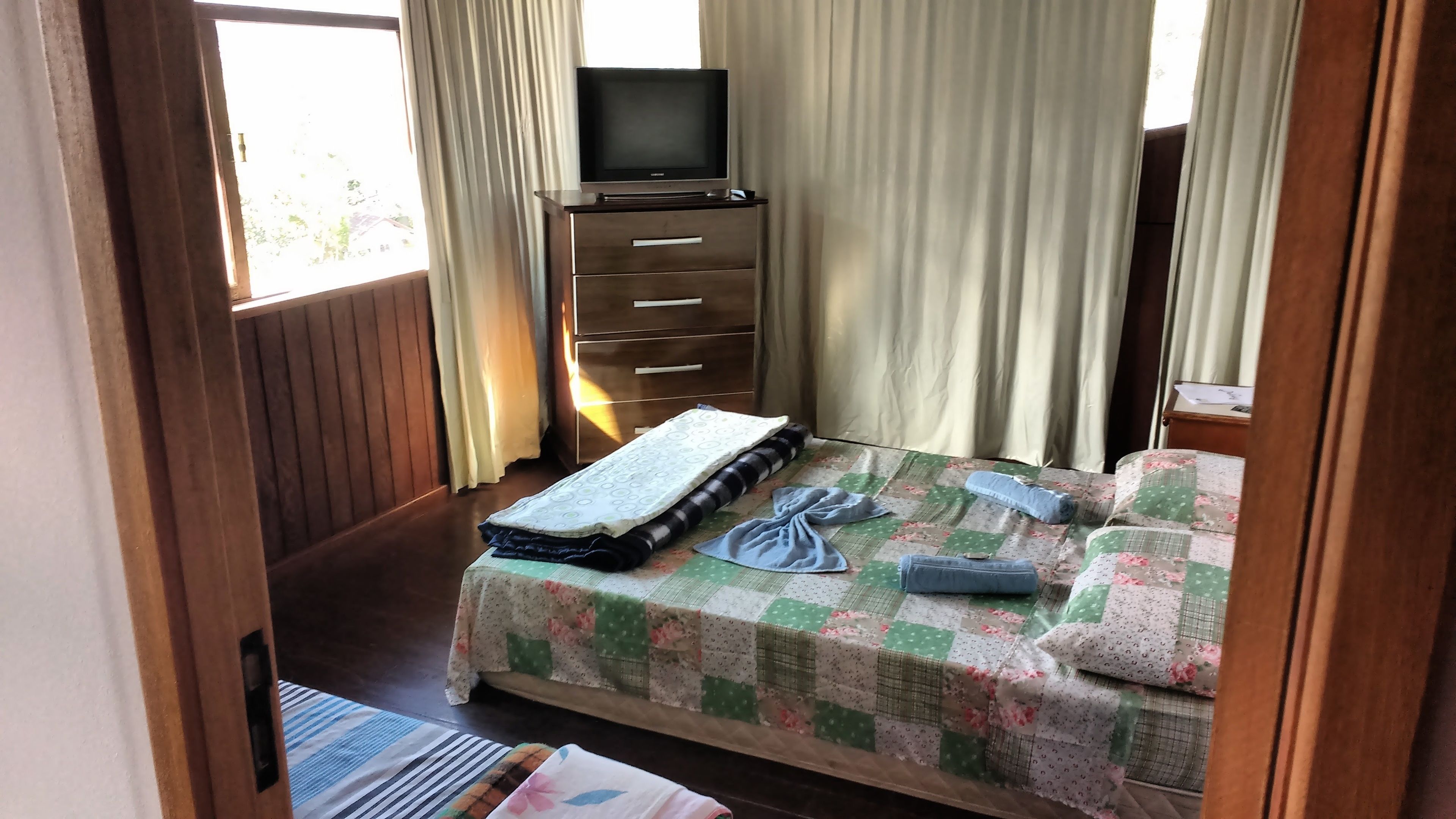 A bedroom with a bed, a TV on a dresser, and a window with curtains.