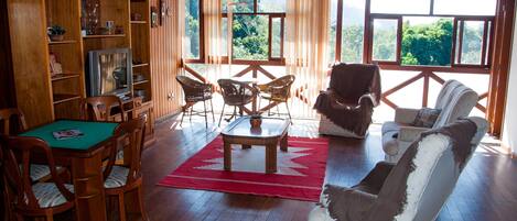 A wooden-paneled room with a dining table, chairs, a sofa, and a television.