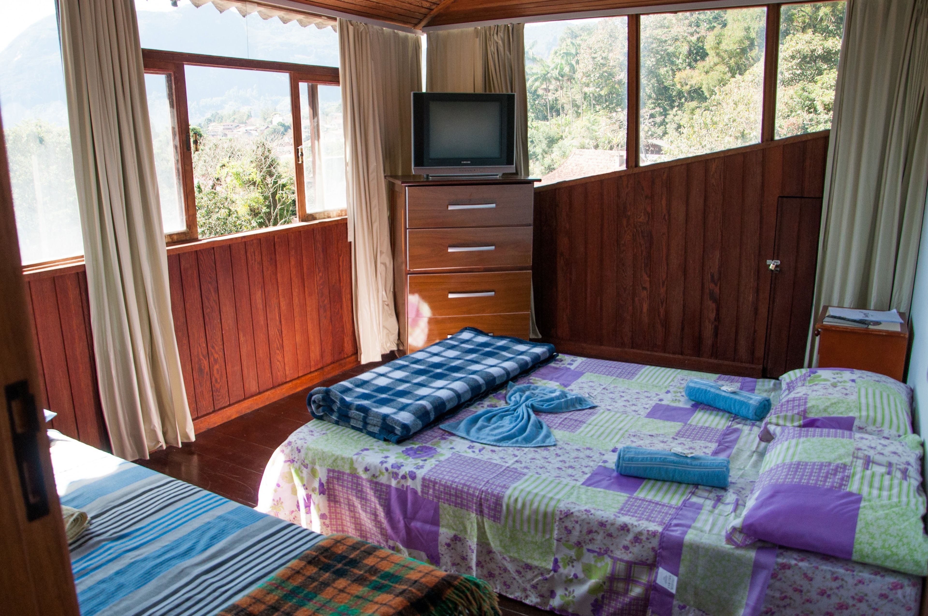 A bedroom with a bed, a TV on a wooden cabinet, and a window with curtains.