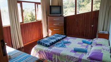 A bedroom with a bed, a TV on a wooden cabinet, and a window with curtains.
