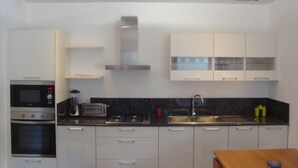A modern kitchen with white cabinets, a built-in oven, a microwave, a toaster, and a sink. - Ernaa Chambres D'Hotes (Abidjan)