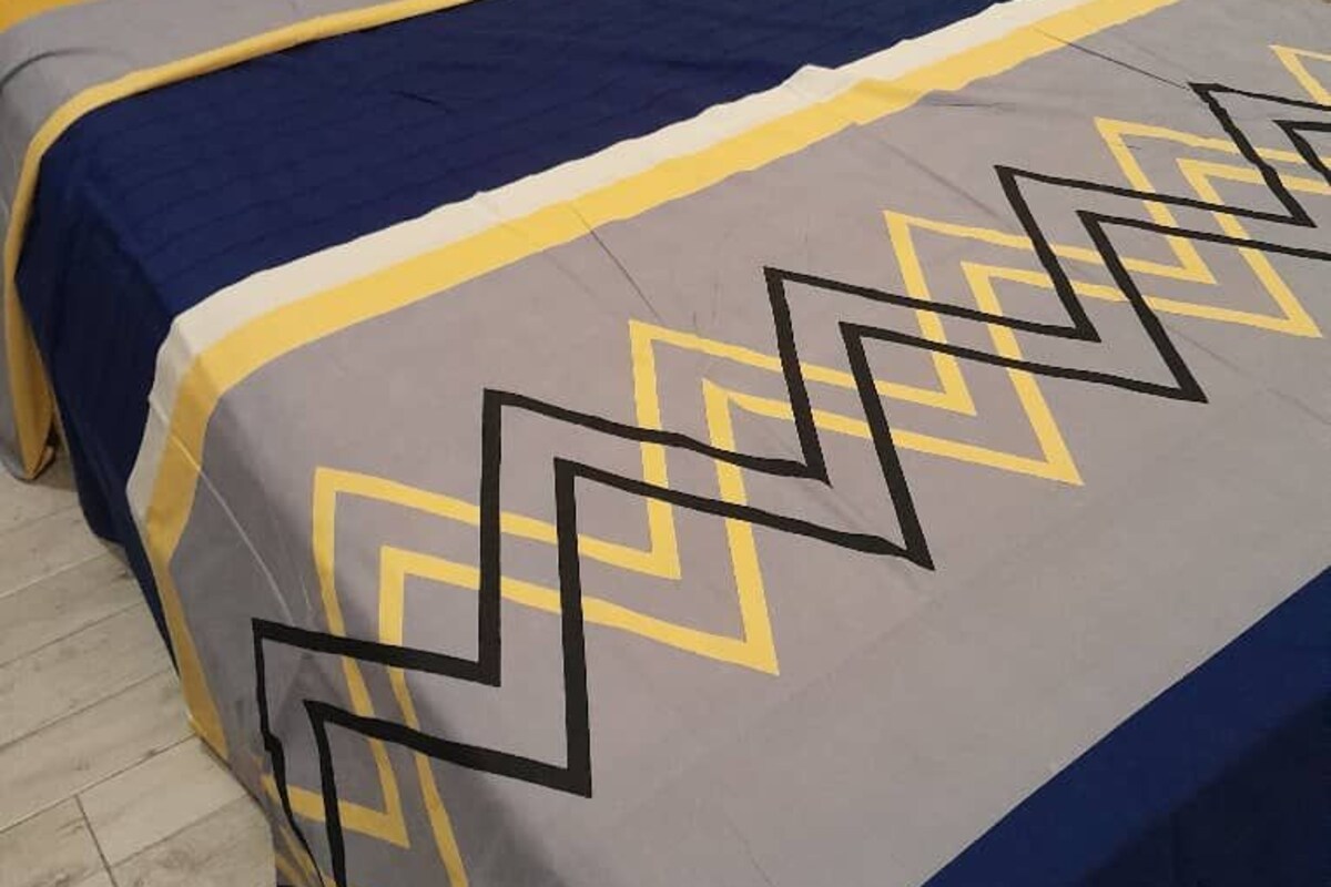 Una cama con una colcha de diseño geométrico en tonos azul, amarillo y gris.