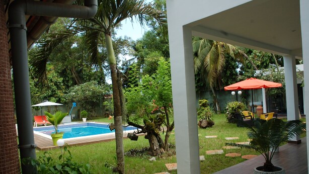 A pool area with a clear view of the surrounding garden, including palm trees and a well-maintained lawn. - Ernaa Chambres D'Hotes (Abidjan)