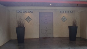 A building entrance with a decorative door, two potted plants, and a tiled floor. - Ernaa Chambres D'Hotes (Abidjan)