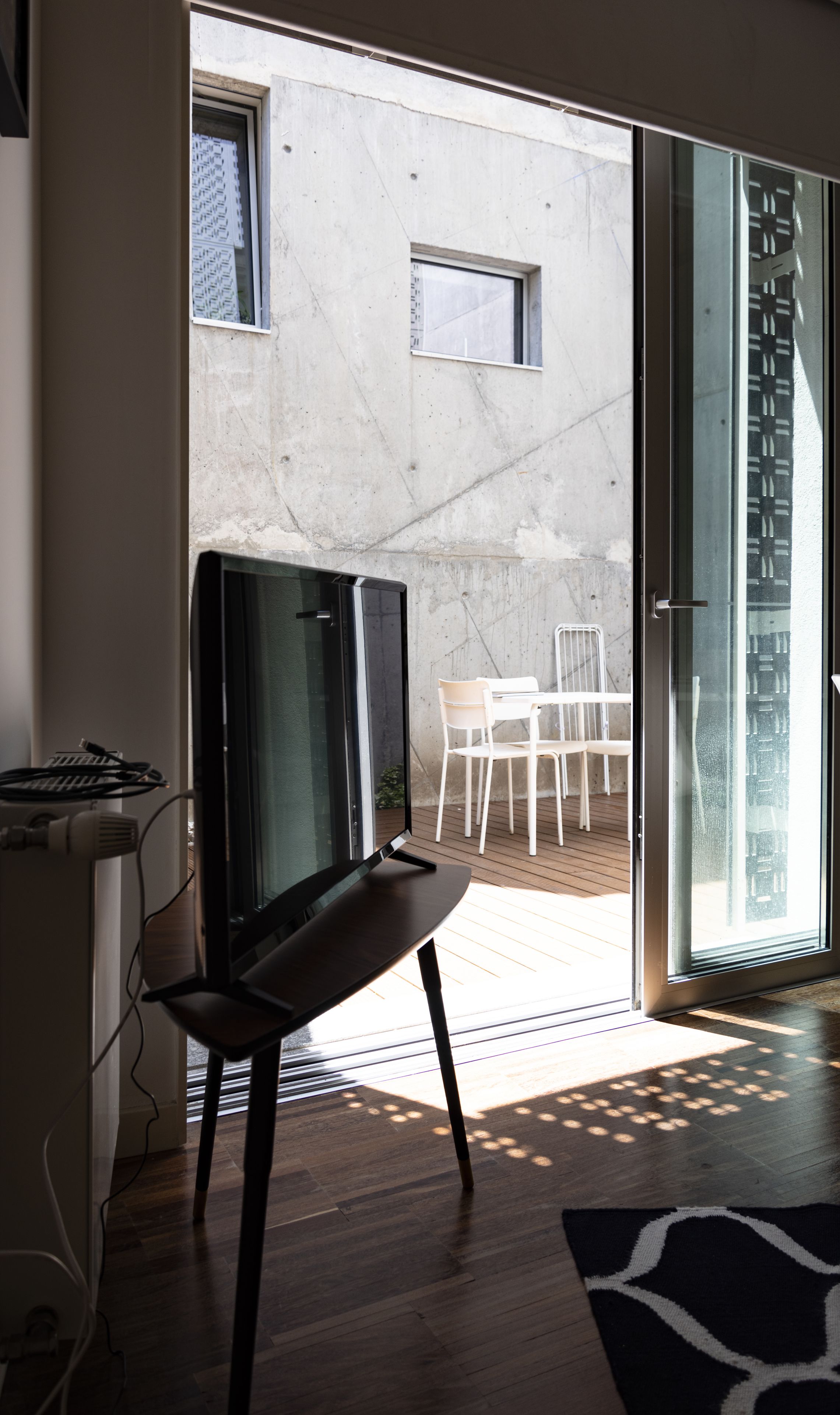 Uma sala de estar moderna com televisão, um espaço de jantar com cadeiras e um acesso direto a um pátio externo por meio de uma porta de vidro deslizante.