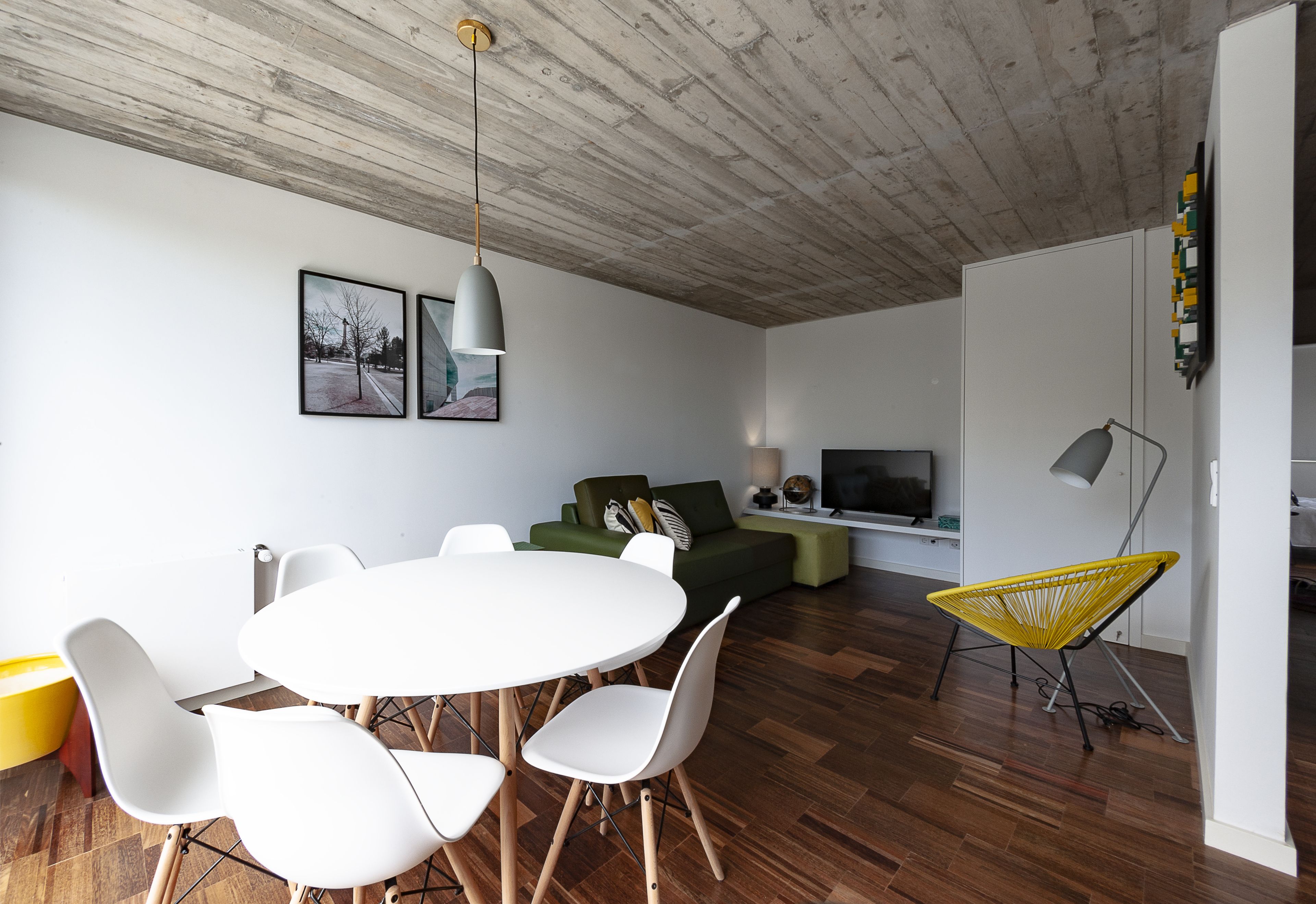 Una sala de estar moderna con techo de madera, una mesa de comedor con sillas, un sofá, un sillón amarillo y un televisor.