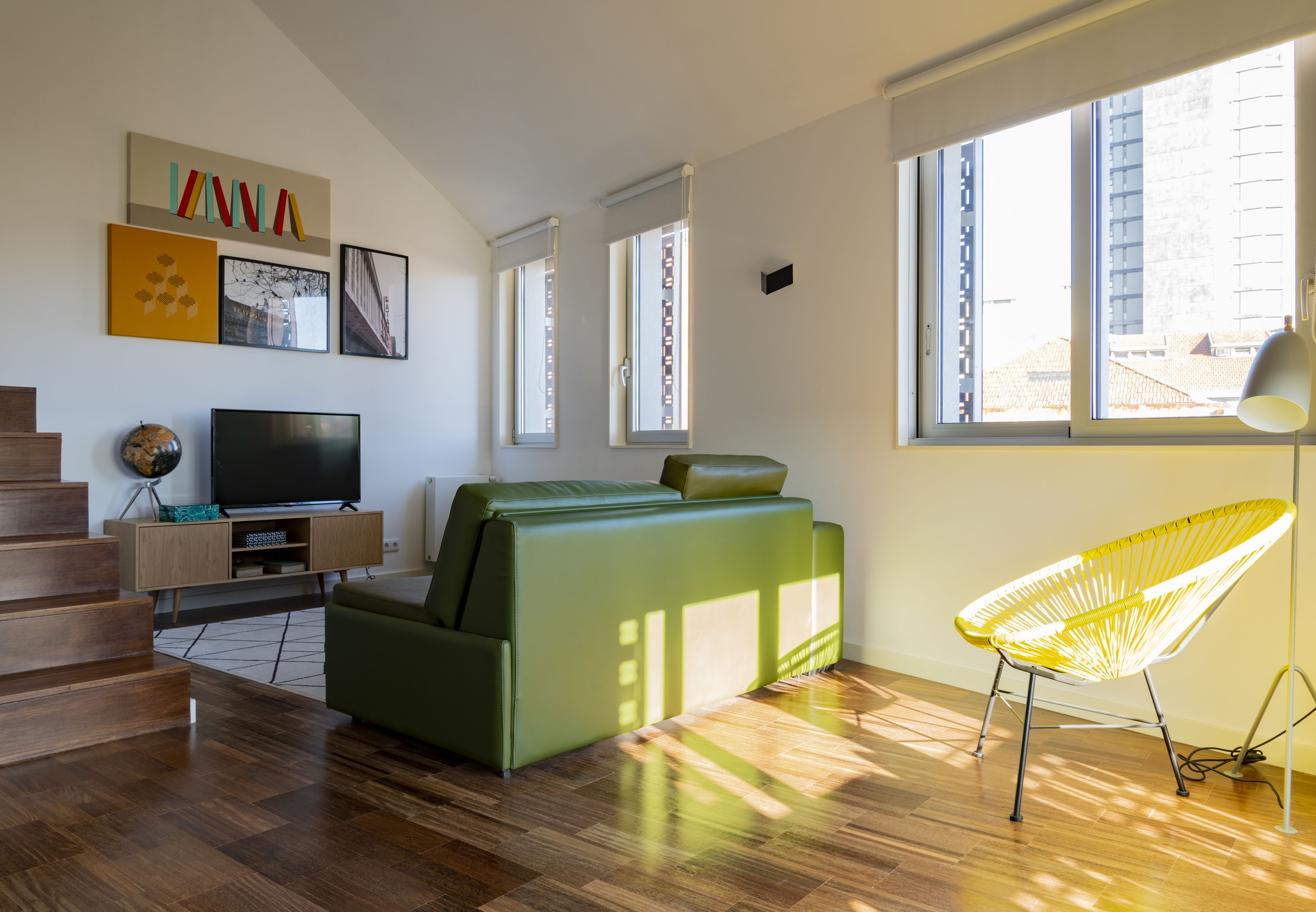 A modern living room with a green sofa, a yellow chair, a flat-screen TV, and artwork on the wall.