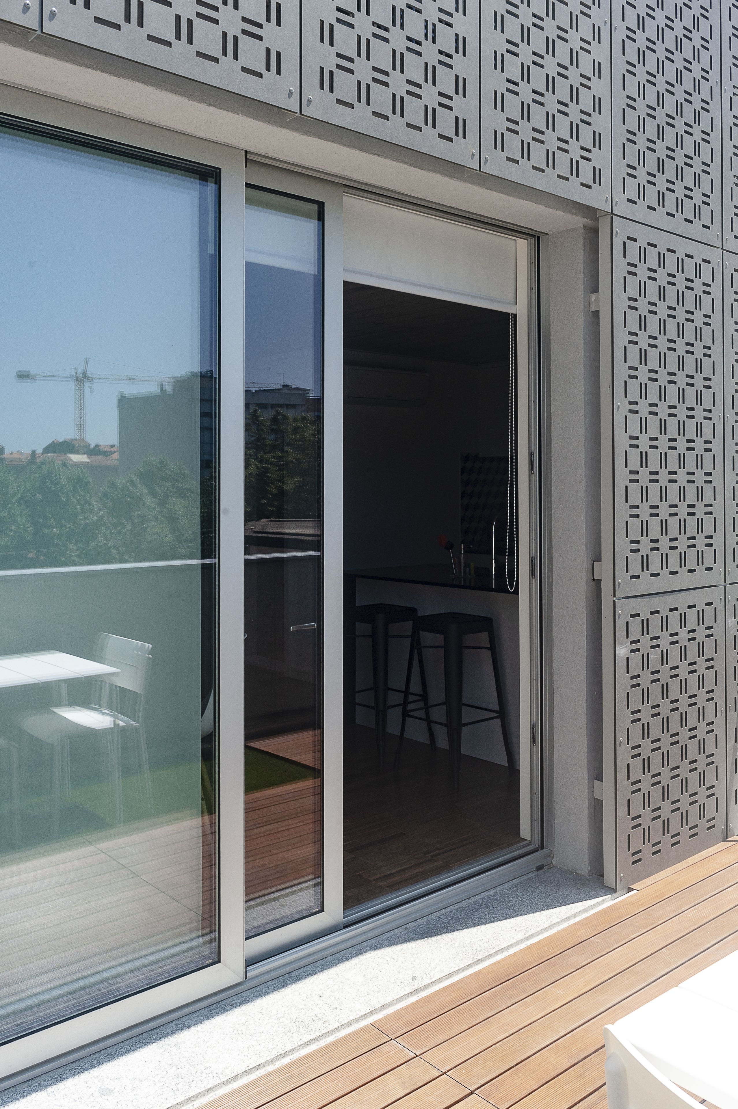 A modern building with a sliding glass door leading to an outdoor area with a wooden deck and two bar stools.