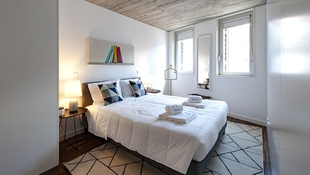 A modern hotel room with a wooden ceiling, a large bed with a geometric-patterned rug, a bedside table with a lamp, and a wall-mounted artwork. - PortoSoul Trindade (Porto)