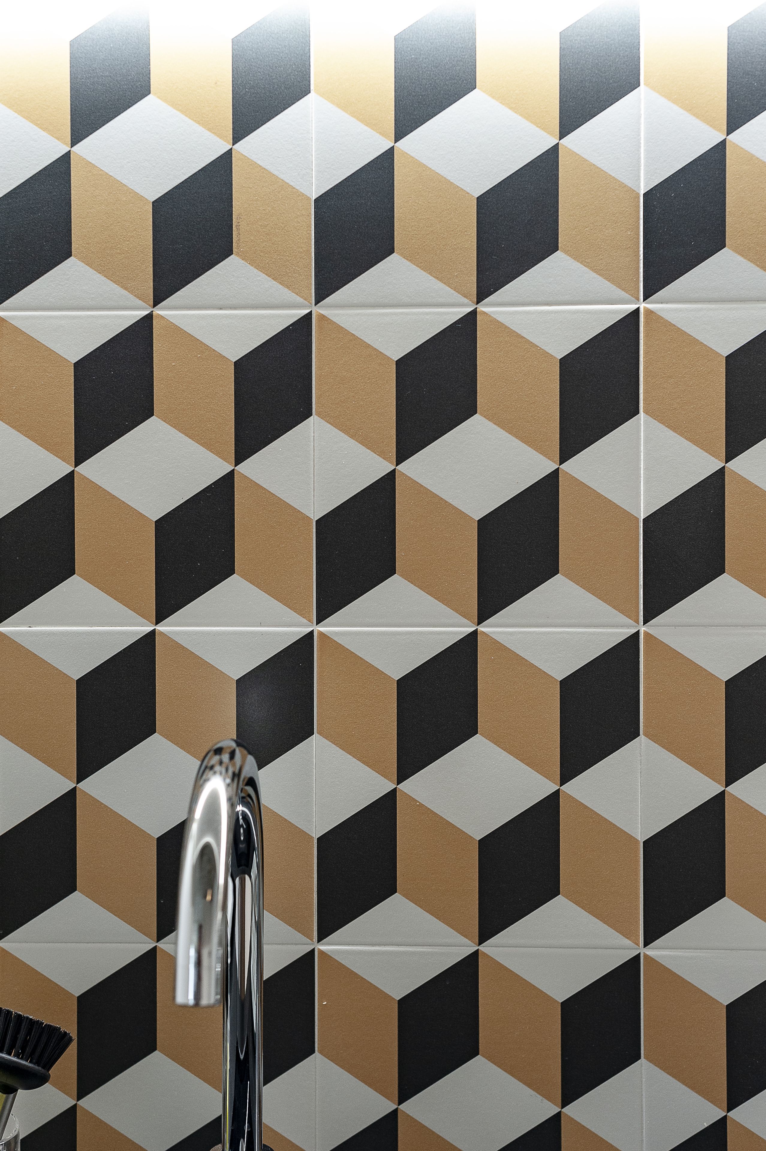 Ein Badezimmer mit Wandfliesen in geometrischem Muster und einem Chromarmaturen.