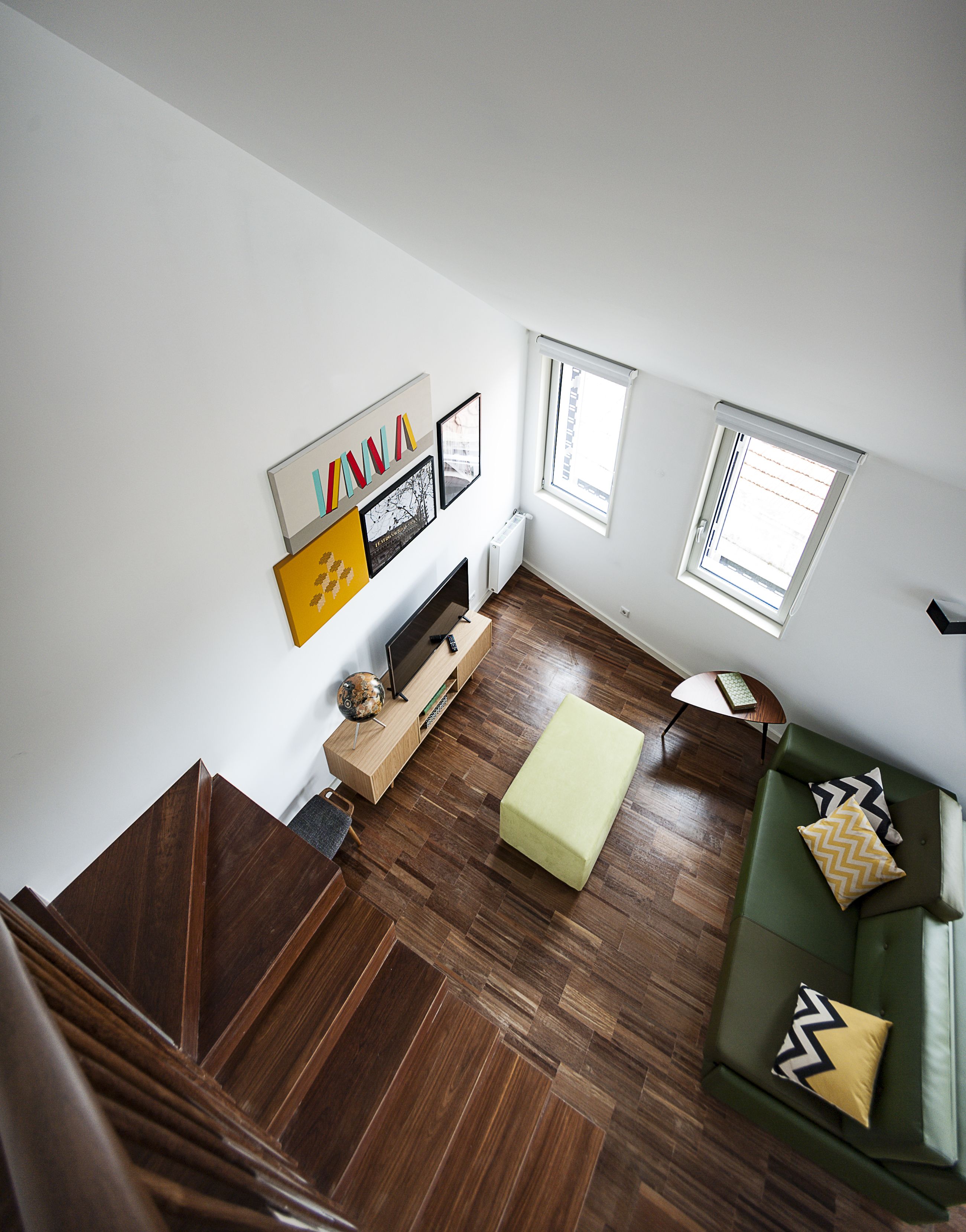 Un salon moderne avec un plancher en bois, un canapé vert, une petite table et un téléviseur posé sur un meuble en bois.
