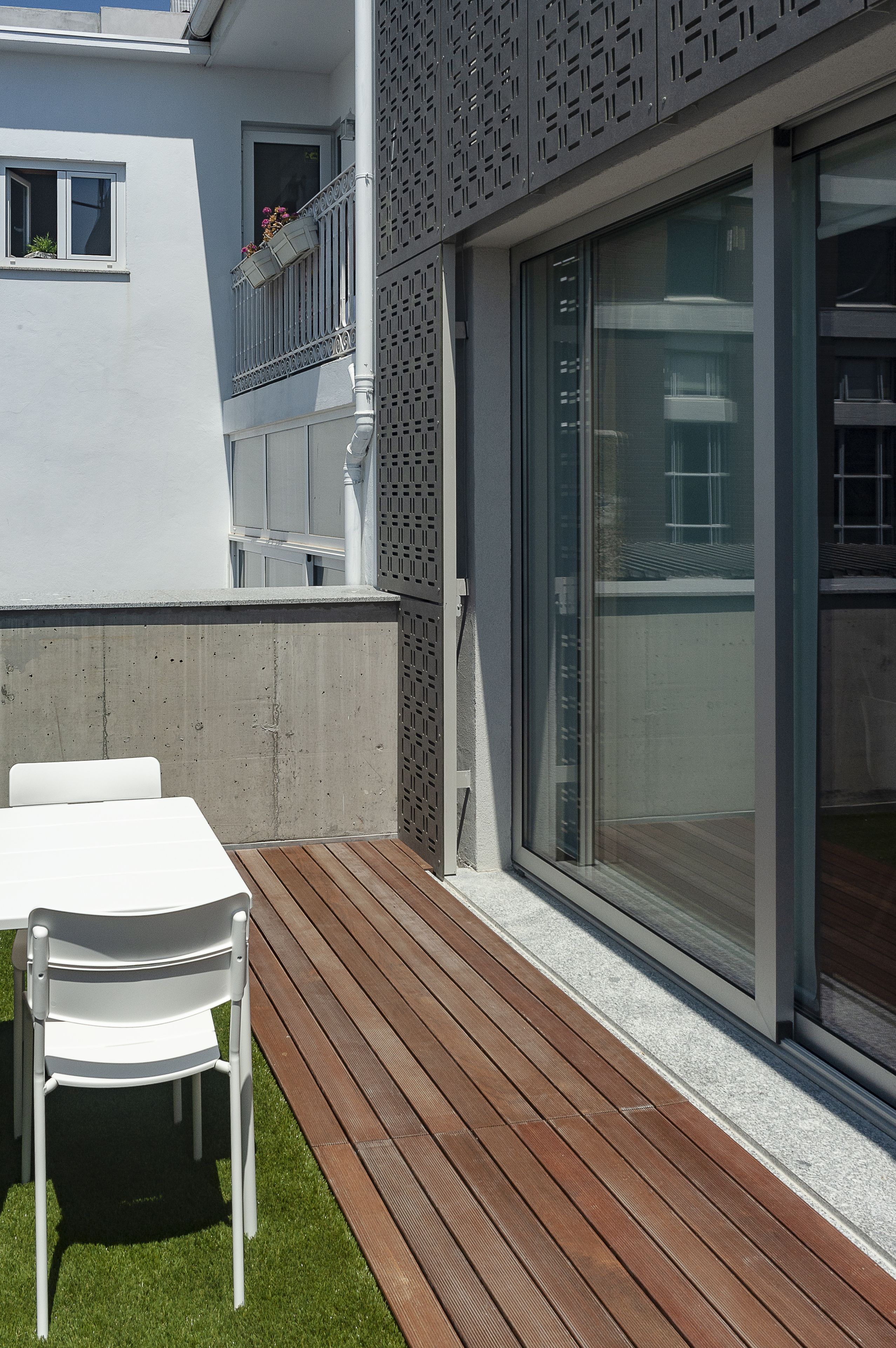 Eine moderne Terrassenanlage mit Holzboden, weißer Möbel und einer Betonwand.