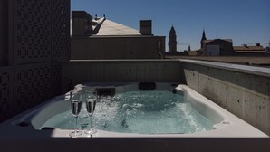 A hot tub with two glasses of water, a patterned wall, and a view of a building with a clock tower in the background. - PortoSoul Trindade (Porto)