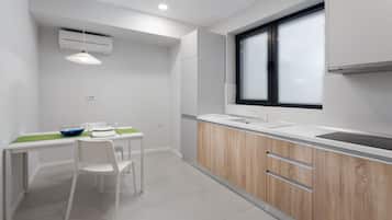 A modern kitchen with white cabinetry, a wooden countertop, and a window with blinds.