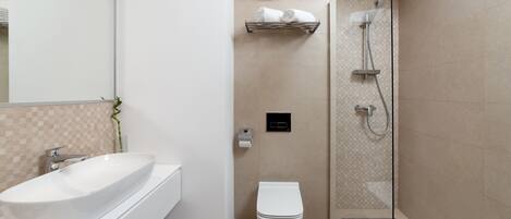 A modern bathroom with a large white sink, a toilet, a glass-enclosed shower, and a towel rack.