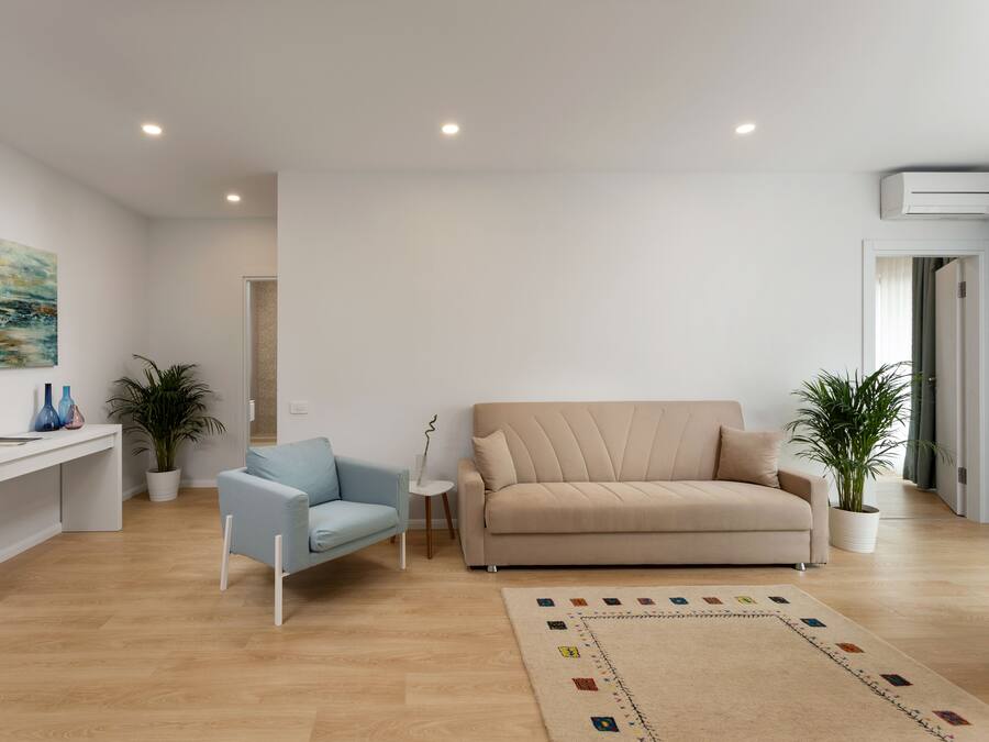 A modern living room with a light blue armchair, beige sofa, white console table, and a colorful rug.