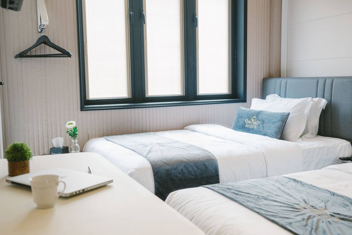 Habitació d'hotel amb dos llits, una taula de treball amb un ordinador portàtil, una tassa i una petita planta.