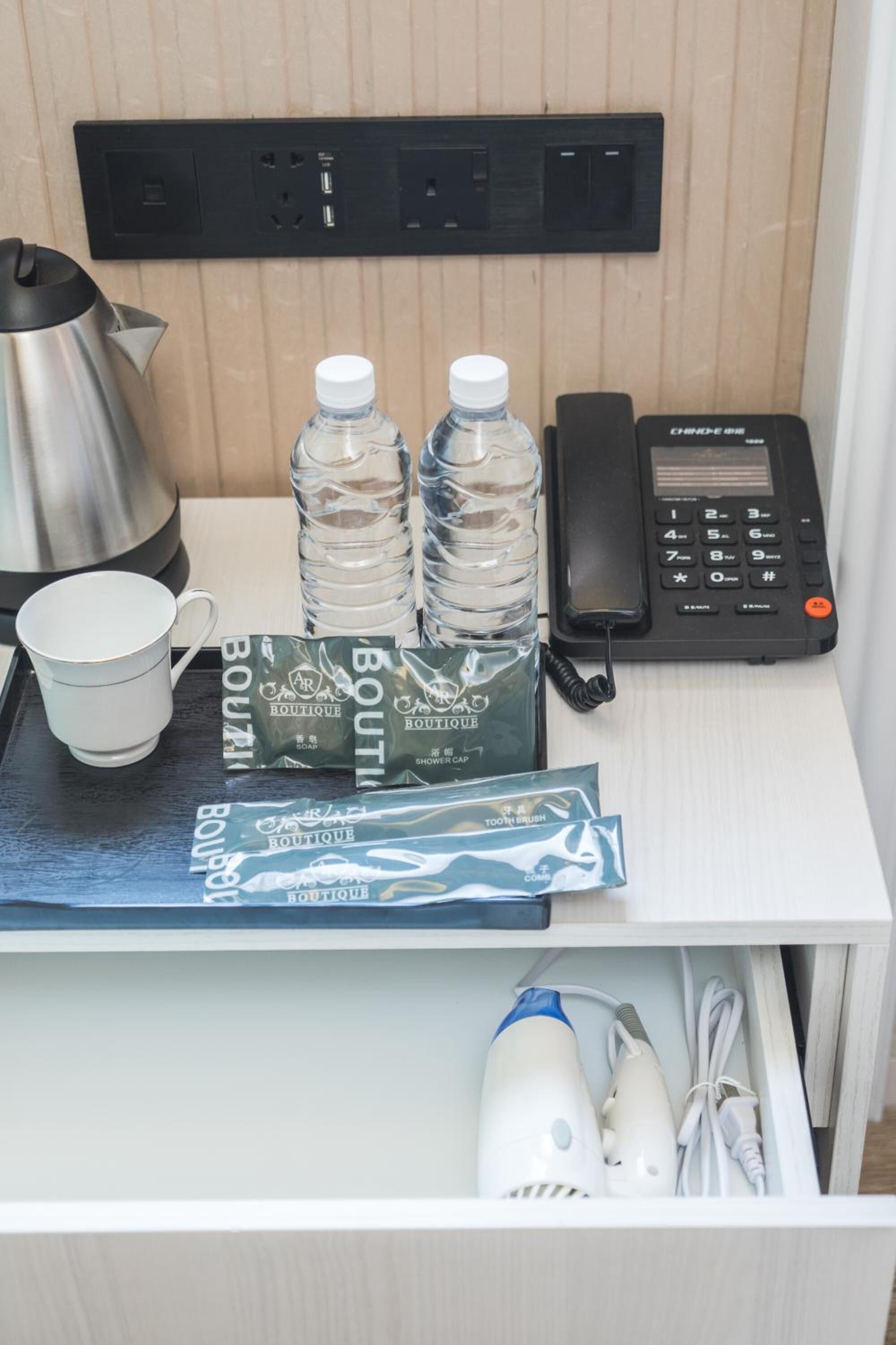 A hotel room with a minibar, a kettle, bottled water, a phone, and toiletries.