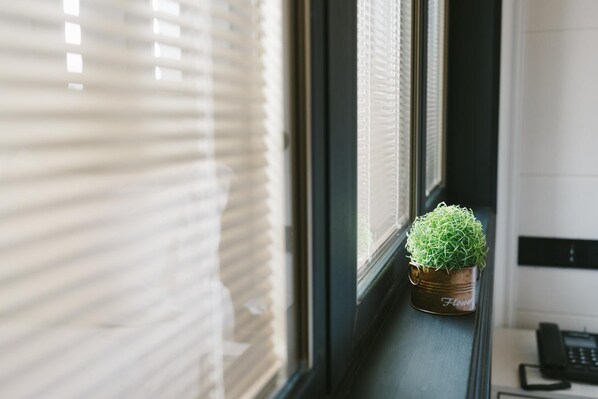 Une fenêtre avec des stores, une petite plante en pot sur le rebord et un téléphone sur un bureau.