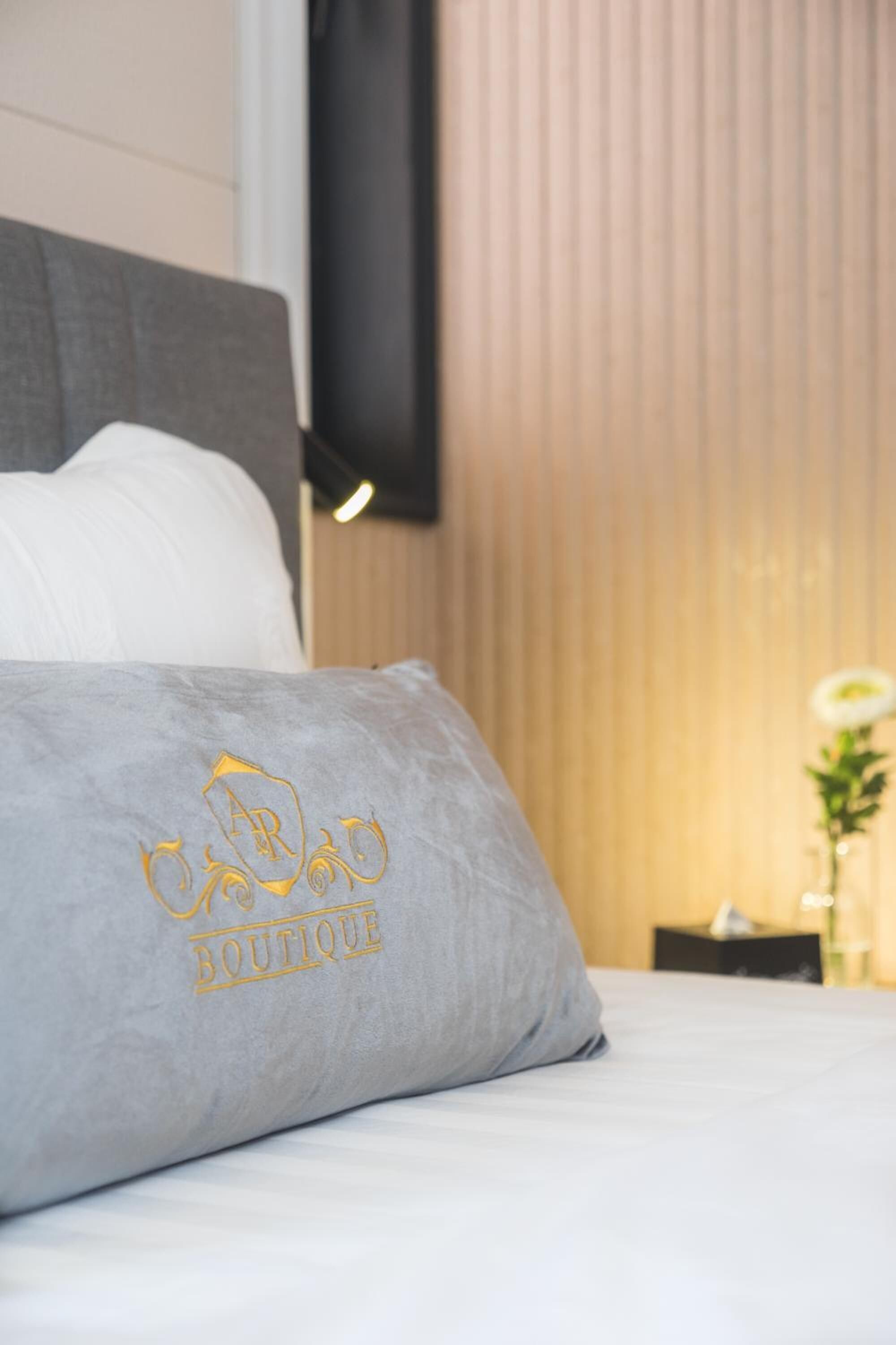 A neatly made bed with a grey pillow featuring a logo and the word "BOUTIQUE".