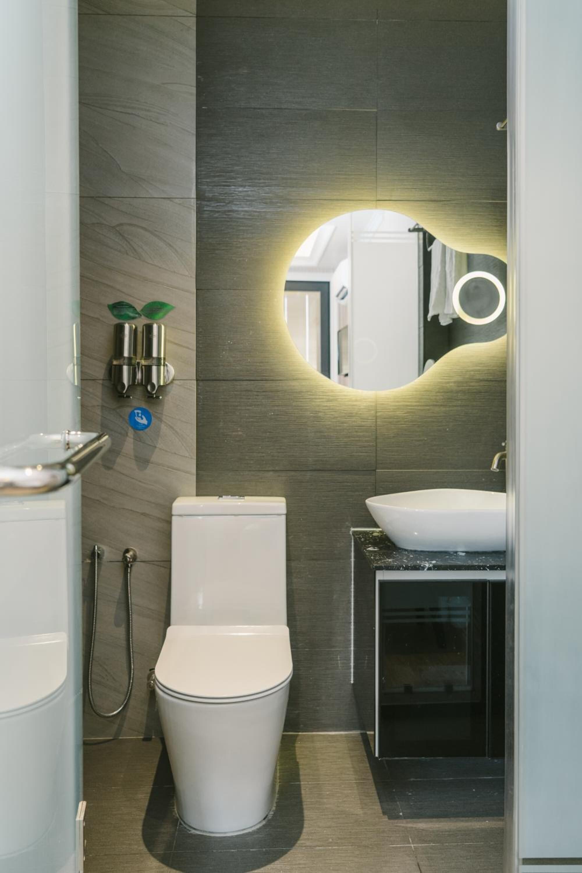 A modern bathroom with a toilet, sink, and a mirror with a circular light.