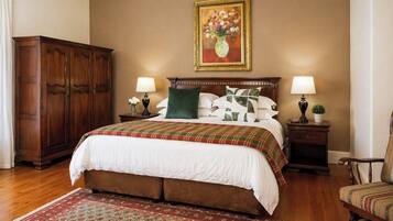 A bedroom with a large bed, two bedside tables with lamps, a wooden wardrobe, a painting on the wall, and a patterned rug.