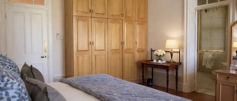 A bedroom with a bed, wooden wardrobe, a bedside table with a lamp, and a view of a bathroom through an open door.