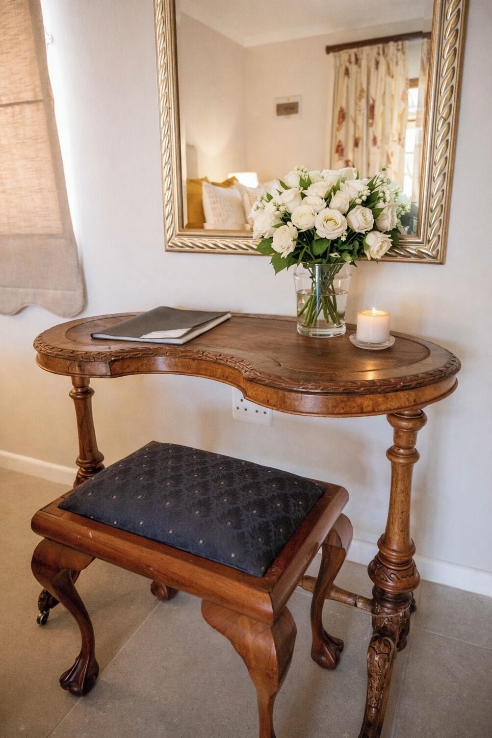 Un banco de madera con asiento acolchado, una mesita con una vela y un jarrón de flores blancas.