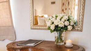 A wooden bench with a cushioned seat, a small table with a candle, and a vase of white flowers. - Bakenskraal Ostrich Palace (Oudtshoorn)