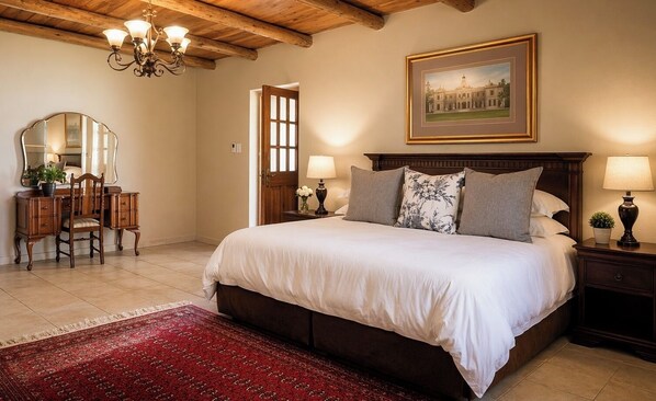 A bedroom with a large bed, a wooden desk, a chair, a chandelier, a painting, and a red carpet. - Bakenskraal Ostrich Palace (Oudtshoorn)