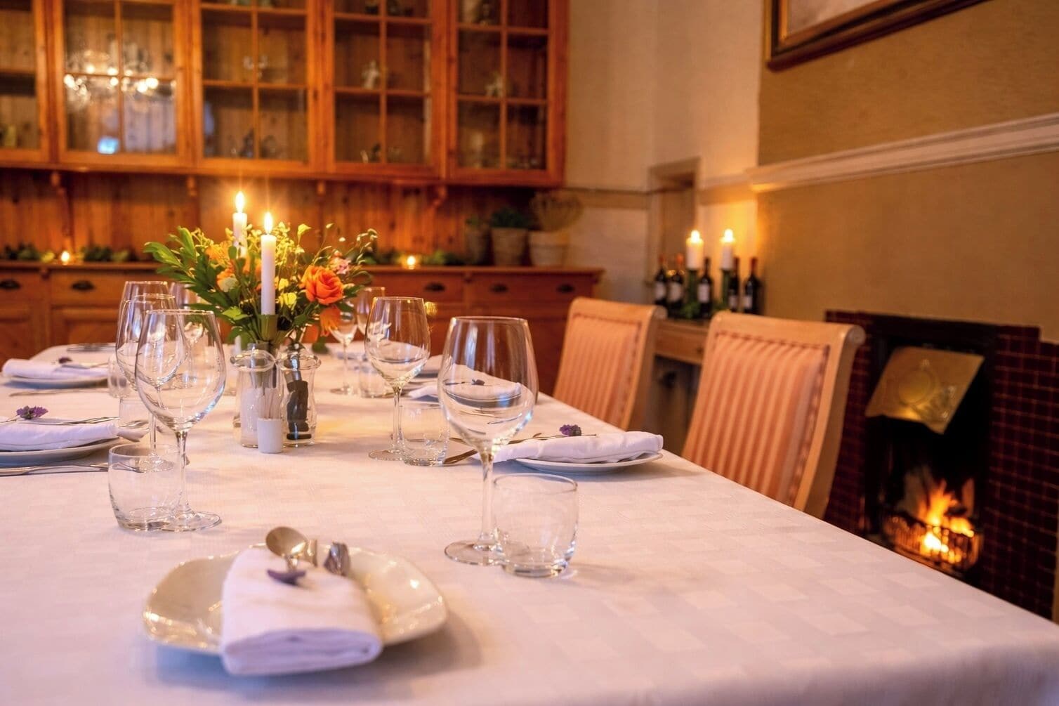 A dining table set for a meal with candles, glasses, and a vase of flowers.