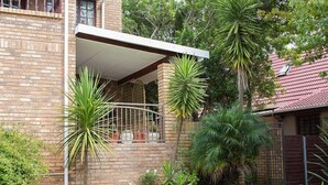 Ein Ziegelhaus mit überdachter Terrasse, umgeben von verschiedenen tropischen Pflanzen.