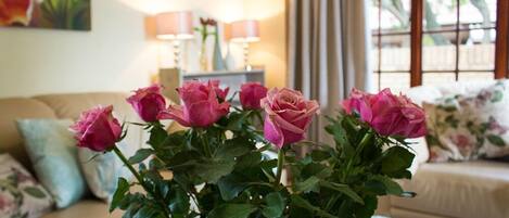 A living room with a floral arrangement of roses in a vase, a sofa with floral cushions, and a lamp on a side table.