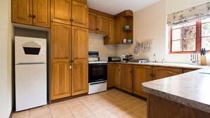 Eine Küche mit Holzausstattung, einem weißen Kühlschrank, einem Backofen und einem Fenster mit Blick auf Bäume.