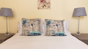 Ein Bett mit zwei dekorativen Kissen mit Schmetterlingsmotiven, seitlich von je einer Lampe eingerahmt.