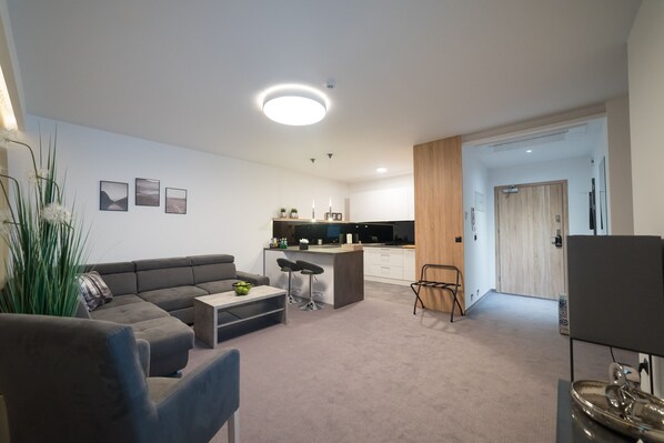 A modern living room with a sofa, coffee table, and a small dining area. There is a kitchen area with a countertop and cabinets.