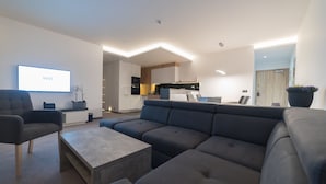 A modern living room with a large sectional sofa, a coffee table, and a flat-screen TV mounted on the wall. - Apart-Hotel VIVI Residence & SPA (Zory)
