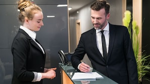 Two people in business attire at a reception desk with a phone and papers. - Apart-Hotel VIVI Residence & SPA (Zory)