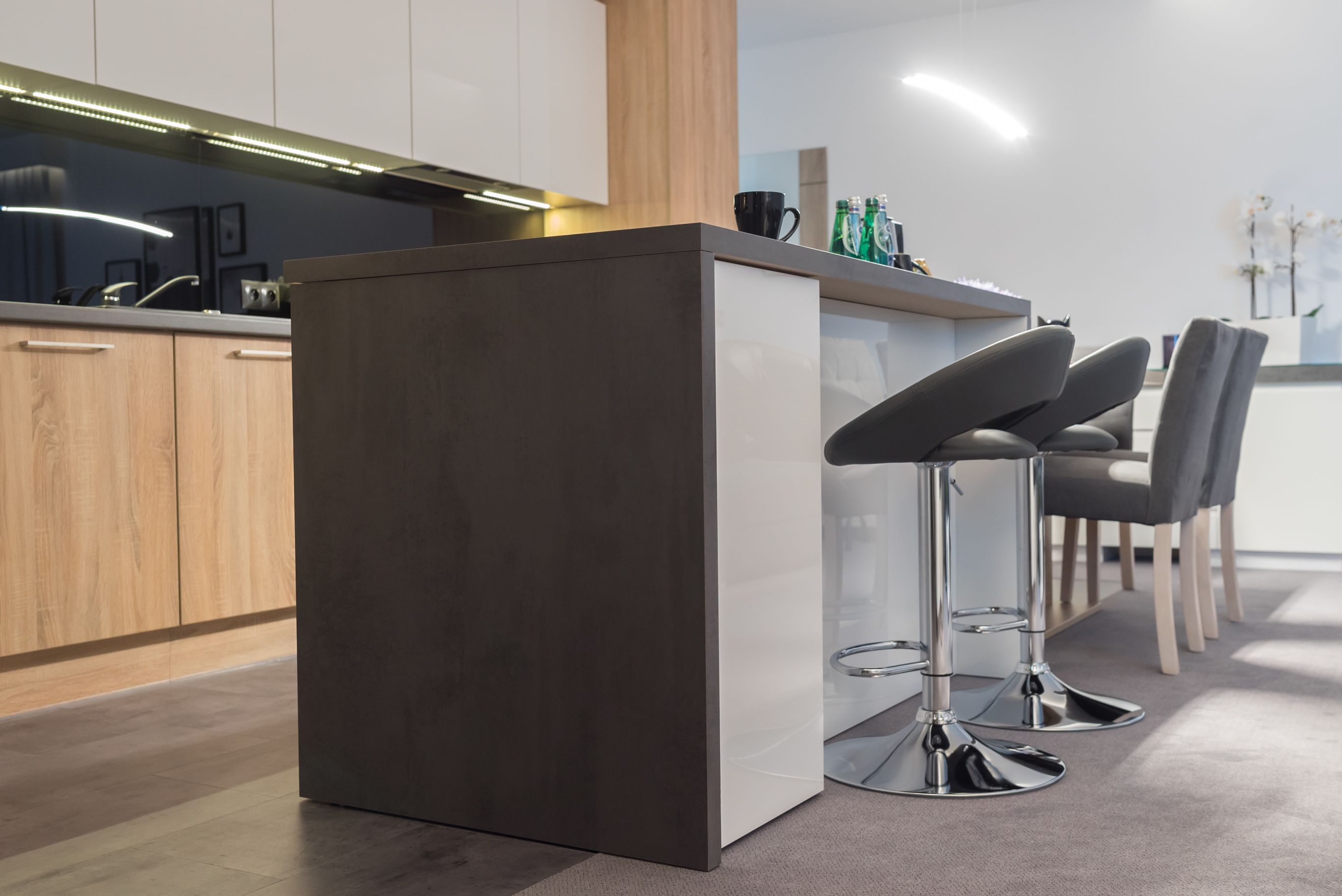 A modern kitchen with a central island, bar stools, and a countertop with bottles.