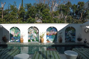 A pool area with tiled flooring, a seating area with striped cushions, and four arched windows with mosaic artwork.