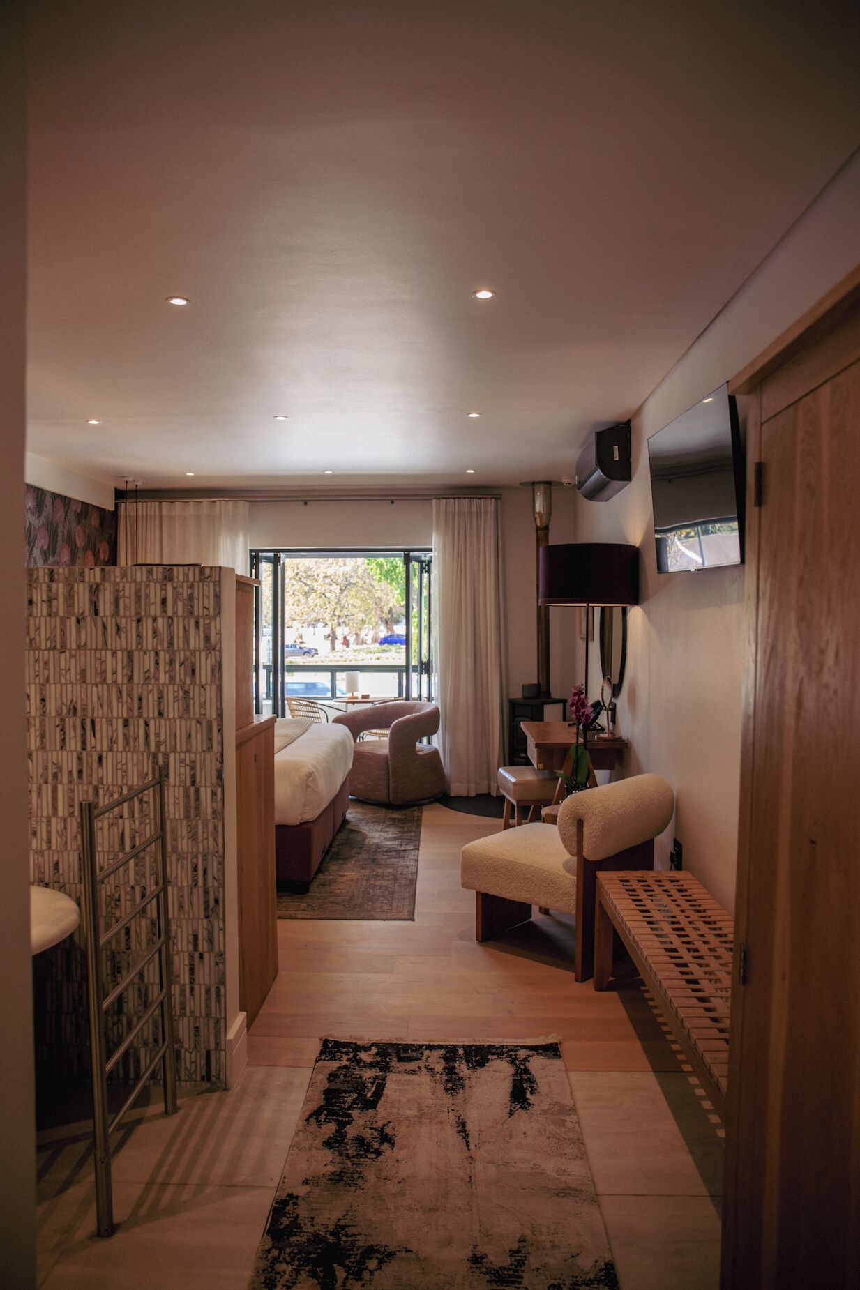 A hotel room with a bed, seating area, TV, and a view of the outdoors.