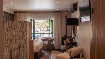 A hotel room with a bed, seating area, TV, and a view of the outdoors.